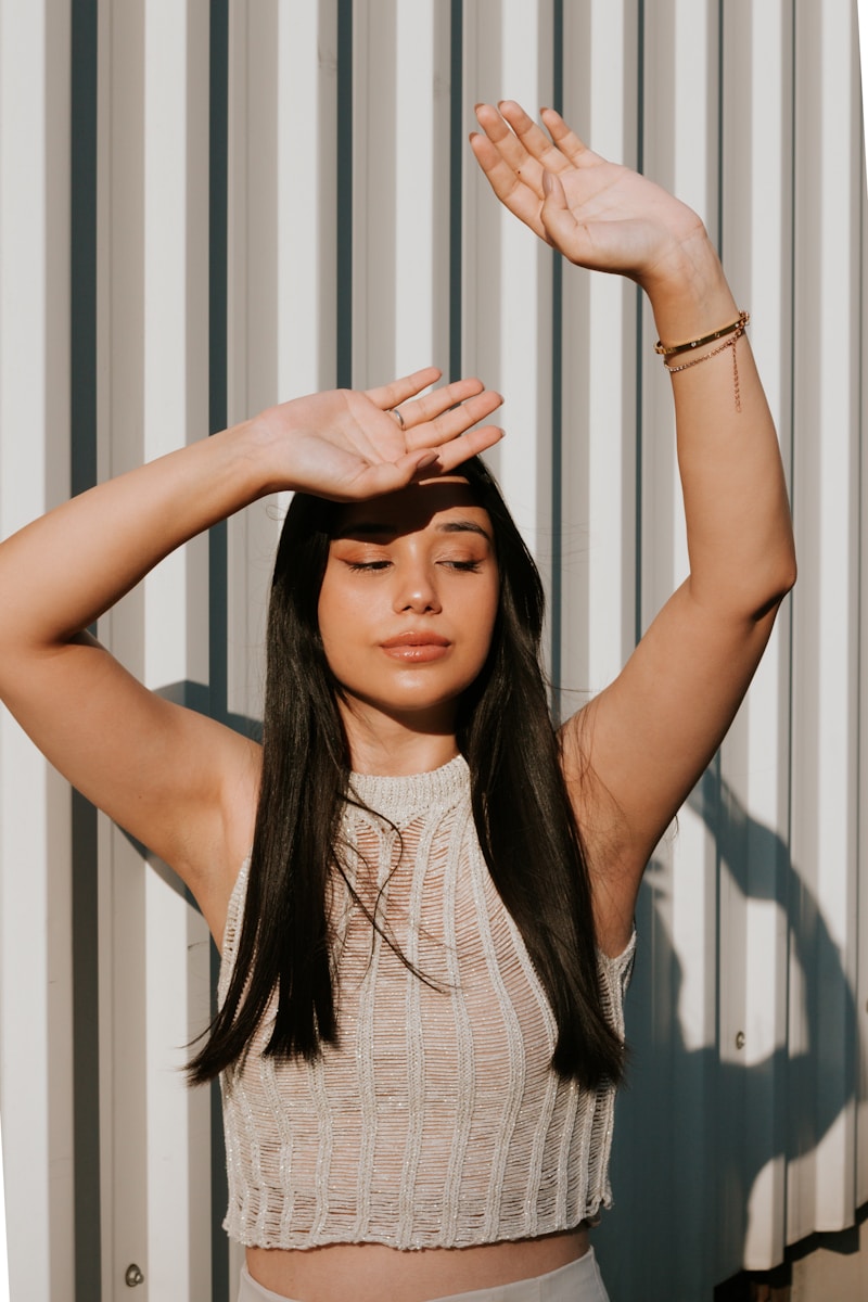 A woman standing in front of a wall with her hands on her head